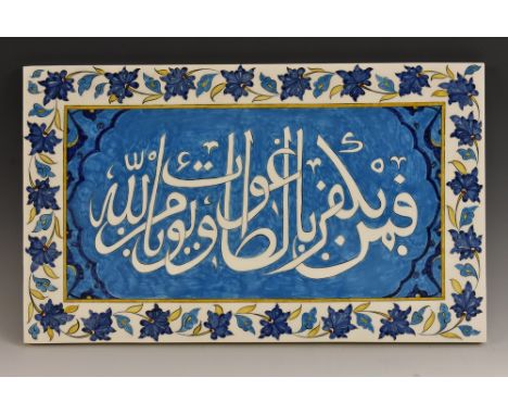 A large Middle Eastern rectangular tile, in the Iznik taste, inscribed in Arabic on a turquoise ground, within a border of fl
