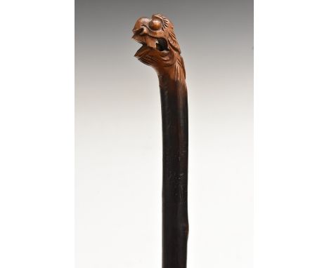 A novelty softwood walking stick, the carved grotesque mask grip enclosing a 'puzzle' ball, gnarly shaft, 102cm long, early 2