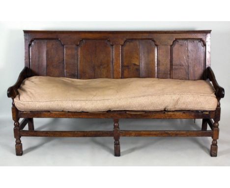 An oak coaching settle, first half 18th century, the back with four fielded arch top panels, above a later strung seat frame 