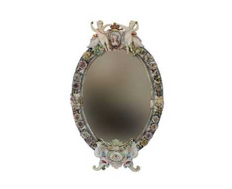 A large oval porcelain florally encrusted mirror, in Meissen style, 19th century, the bevelled oval plate surmounted by a por