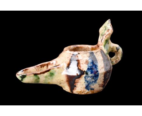 Ca. 1100-1200 AD.A pottery oil lamp featuring an elegant cream glaze adorned with alluring splashes of brown, green, and blue