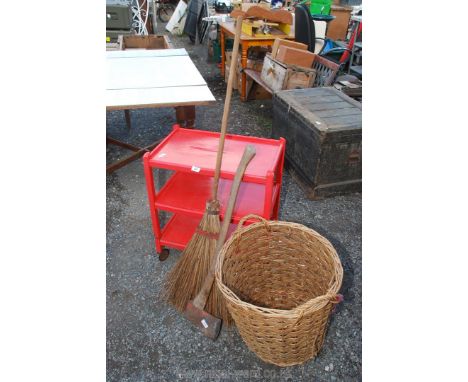 A red painted 3 tier trolley on castors, wicker basket, axe and broom.