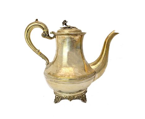 A silver teapot, decorated with a central band, having a scrolling handle, flower finial to the lid and raised on four shell 