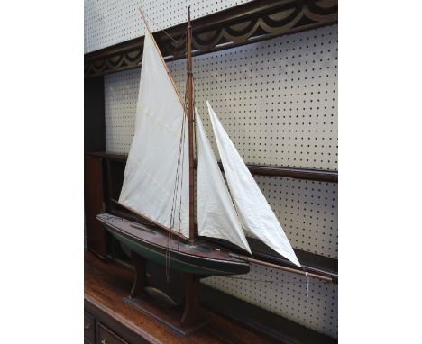 A vintage wooden pond yacht with black and green painted hull and lead weighted shaped keel, on a mahogany stand, 116cm wide 
