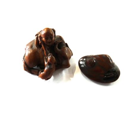 A Japanese wood netsuke of a man seated on a recumbent buffalo, 19th/20th, leaning over to tickle the chin of a young animal,