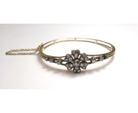 A diamond set oval hinged bangle, the front with a flowerhead motif, between diamond set three stone sides, mounted with cush