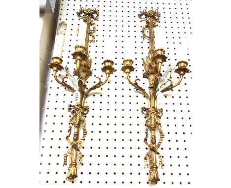 A pair of gilt bronze three branch wall appliques of Louis XVI style, early 20th century, with ribbon tie and torchère backpl