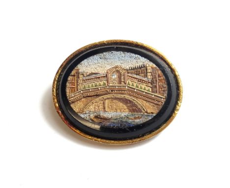 A gold mounted oval micro-mosaic brooch, designed as a river scene with a bridge, within a decorated gold surround, length 4.