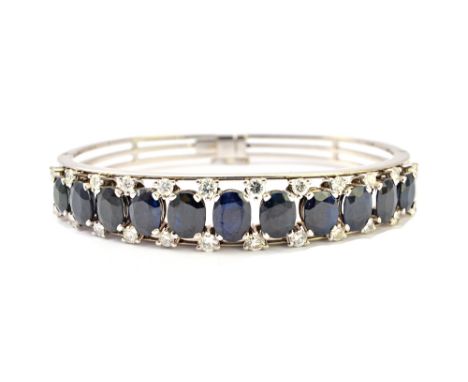 A sapphire and diamond set oval hinged bangle, the front mounted with a row of eleven oval cut sapphires graduating in size t