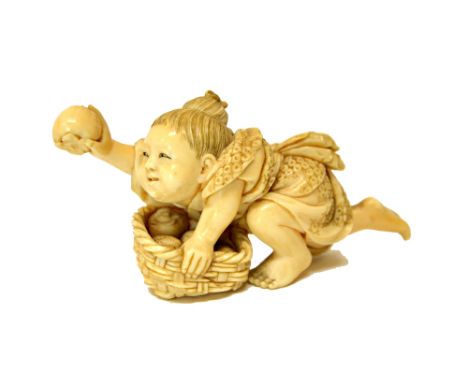 A Japanese ivory netsuke of a child, Meiji period, crouching over a basket of fruit and holding a single fruit in his outstre