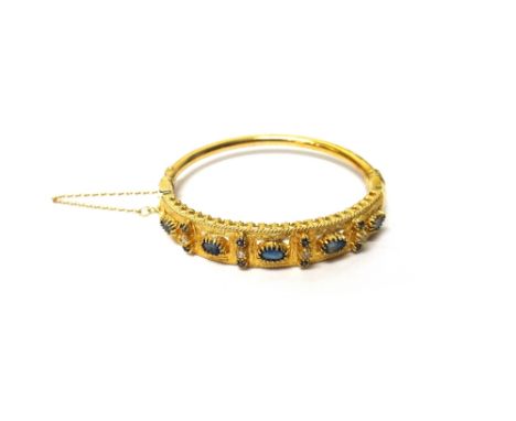 A gold, sapphire and diamond set oval hinged bangle, the front mounted with five oval cut sapphires and with four diamond and