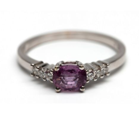 18 kt. Witgouden ring, centraal bezet met een roze saffier van 6 x 5 mm, geflankeerd door briljant geslepen diamanten (totaal