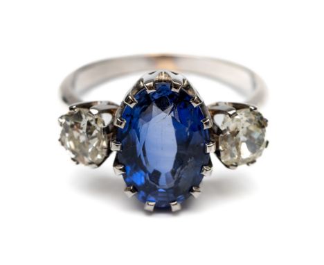 18 kt. Witgouden driesteens ring, bezet met een blauwe ovale gefacetteerde saffier van ca. 4.00 ct. (12 x 8,5 mm) geflankeerd