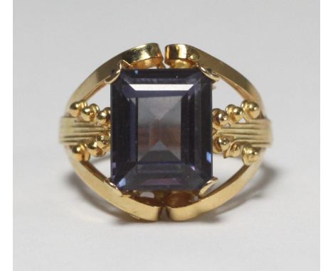 An Egyptian '750' 18ct gold ring of open scrollwork and ball finial design, claw-set with a rectangular stepped cut synthetic