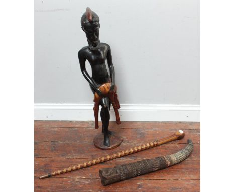 An ethnic carved wooden figure of tribesman with a dead animal over his knee, together with a carved wooden tusk and a walkin