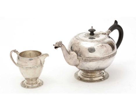 A George V silver teapot and matching milk jug, with applied Celtic knotwork borders and bosses, the teapot with an animal ma