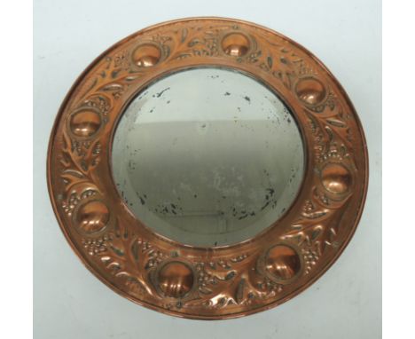 An Arts and Crafts circular copper framed wall mirror, the frame embossed with foliage and circular bosses and with bevelled 