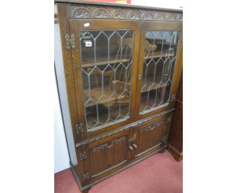 An Oak Book Cabinet, with half wheel carving, honeycomb lead glazed doors, over linen fold panelled doors, on bracket feet, 9