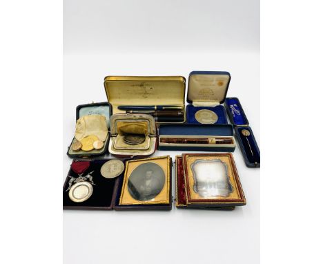 Two framed Daguerreotype portraits in leather cases; a yellow metal stick pin; a quantity of pens and coins; a silver medal. 