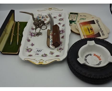Mixed lot to include 2 Goebel Hummel figures, ornate sugar tongs, beermats, tire ashtray, pen set, Royal Albert tray and dice