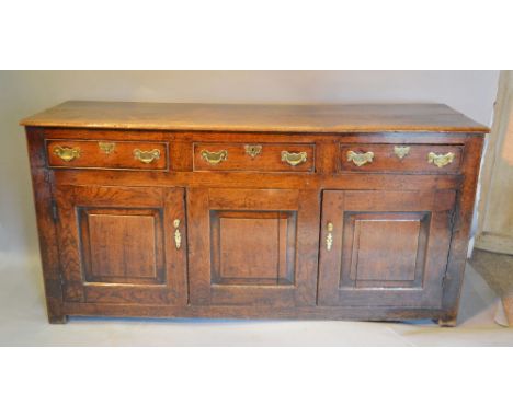 A George III Oak Dresser Base, the moulded plank top above three drawers and two moulded cupboard doors with central panel, a