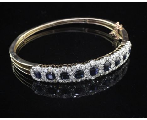 An early 20th century gold, sapphire and diamond hinged bangle, set with nine sapphire and diamond clusters.