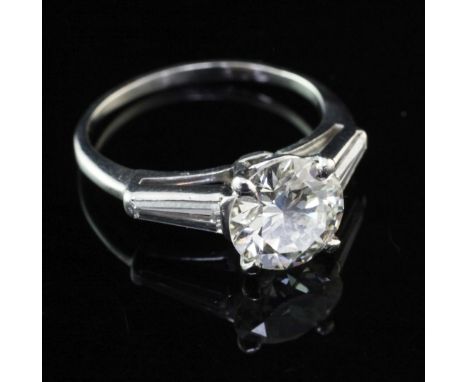 A platinum and single stone diamond ring with trapeze cut diamond set shoulders, the central round brilliant cut stone weighi