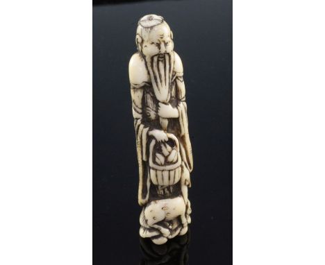 A Japanese stag antler netsuke of a standing sennin, Edo period, holding a basket of peaches with a deer at his feet, 9.8cm