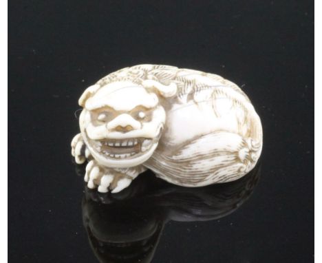 A Japanese ivory netsuke of a shi-shi, Edo period, in recumbent pose, its tail curled around under it's chin, unsigned, 3.6cm