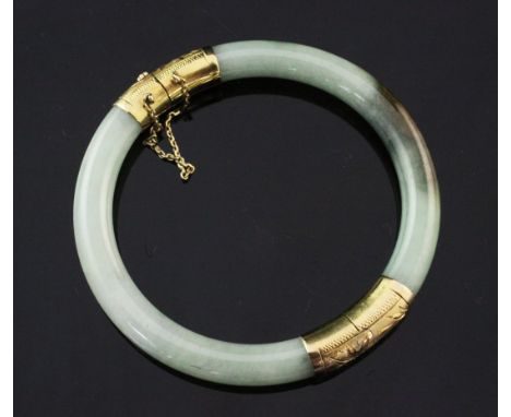 A 14ct gold mounted jadeite hinged bangle, the mounts with engraved decoration.
