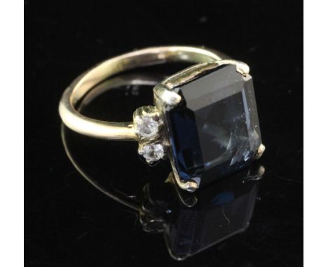 A gold, blue spinel and white sapphire? ring, the emerald cut spinel flanked by two colourless stones, size K.