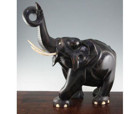 A large Indian ebonised carved hardwood elephant, with ivory tusks, and trunk raised, 21in.