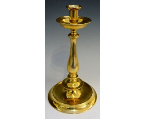 A brass candle stick, the single sconce above drip pan with folded over rim, stem with multiple compressed knops, wide steppe