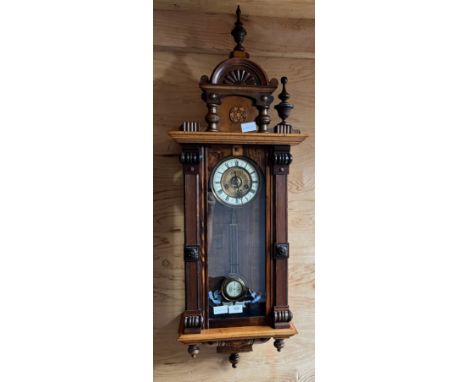Antique ornate wall clock, designed with marquetry trims, Showing a brass face and enamel roman numeral face, Comes with pend