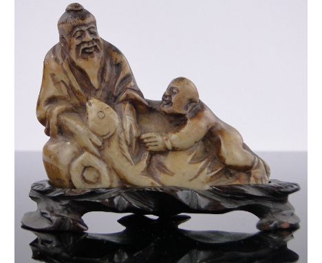 A Chinese carved jade man and boy fishing,length 3.5", carved hardwood stand.