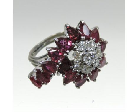An unmarked ruby and diamond cluster ring, of asymmetrical flowerhead design, set with eight central diamonds, within a ruby 