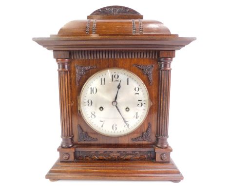 An early 20thC oak cased mantel clock, the circular silvered dial bearing Arabic numerals, eight day, the case carved and rai