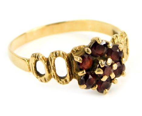 A 9ct gold dress ring, the central garnet cluster claw set, with abstract pierced shoulders, ring size U, 2.1g all in.