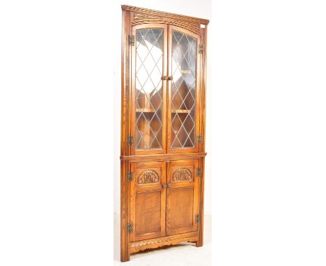 A Wood Bros Old Charm Jacobean revival solid oak corner cabinet. Leaded glass panel doors with enclosed shelves set with cupb