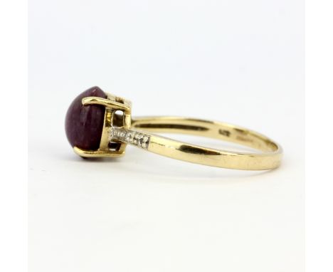 A hallmarked 9ct yellow gold ring set with an oval cabochon ruby and diamond set shoulders, (S).