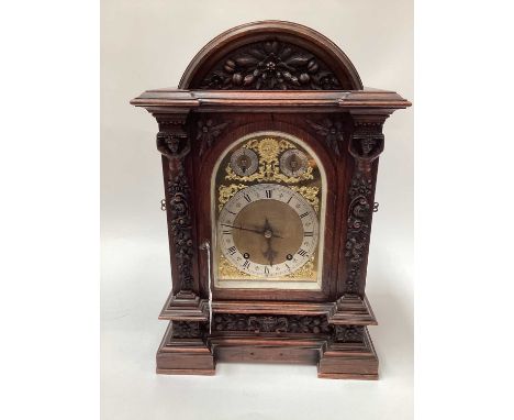 A late Victorian carved oak case chiming mantel clock, the case carved with figural and floral ornamentation, the arched bras