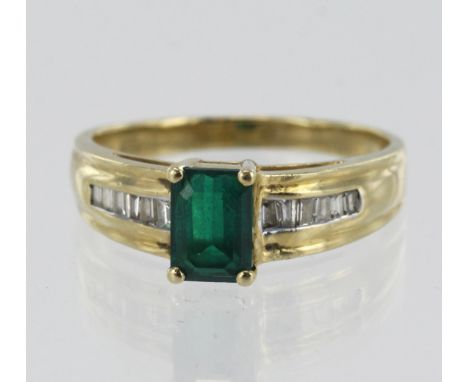 Yellow gold (tests 9ct) diamond and synthetic emerald dress ring, one syn. emerald step cut measuring 7mm x 5mm, flanked with