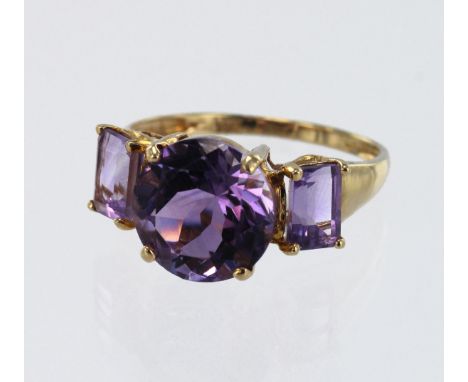 Yellow gold (tests 9ct) amethyst trilogy dress ring, principle round amethyst diameter 10mm, flanked with ne step cut amethys