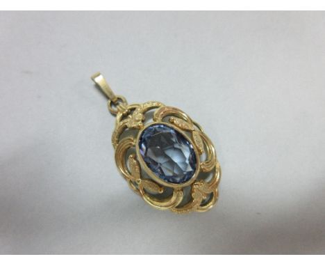 A synthetic light blue spinel pendant, the oval cut spinel collet set to a pierced scrolling and foliate gilt mount with remo