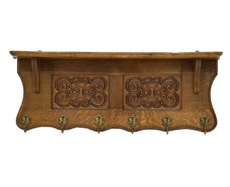Early 20th century carved oak coat rack, the moulded breakfront shelf over two scrollwork panels and six hooks each cast with