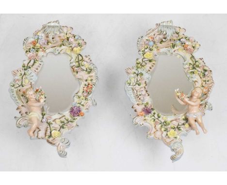 Pair of 20th Century German Sitzendorf porcelain mirrors, each having a shallow-bevelled shaped plate within flower-encrusted