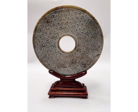 A Chinese Jade coloured hard stone, rounded with wave like carving, with associated wooden stand (ill Fitting), diameter 12cm