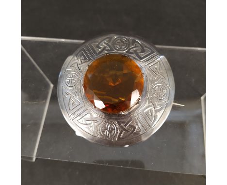 A Scottish silver plaid brooch with engraved Celtic design surrounding a large central orange stone, hallmarked Edinburgh by 