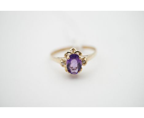 A contemporary amethyst and diamond dress ring, on yellow metal, having an oval cut stone flanked by diamond chips and surrou
