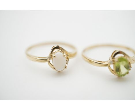 Two yellow metal and gemstone dress rings, one set with an oval cut peridot flanked by diamond chips, the other in opal, both